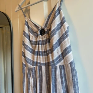 Jumpsuit från Primark - Snygg jumpsuit med smala axelband från Primark. Mjuk och luftig med blå och beige ränder. Har en dekorativ ringdetalj framtill och långa, raka ben. Perfekt för varma dagar när du vill vara både chill och stilren. Står storlek 38 men är mer som en 36. 
