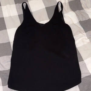 Svart linnetopp med v-ringning - En stilren svart linnetopp med v-ringning och smala axelband. Toppen är ärmlös och har en enkel, clean design som passar till många olika looks. Materialet känns mjukt och lätt, perfekt för varmare dagar eller lager-på-lager.