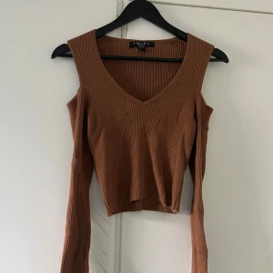 Brun ribbad topp från Amisu - Säljer en brun ribbad topp från Amisu med v-ringning och långa ärmar med slits vid ärmslut. Toppen har en croppad passform och coola cut out-detaljer vid axlarna. Perfekt för dig som gillar trendiga och unika plagg!