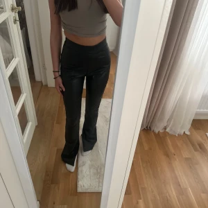 Svarta bootcut byxor i skinnimitation XS -  byxor från NLY Trend i skinnimitation. Hög midja, bootcut-modell med slits nertill på benen och tight passform upptill. 