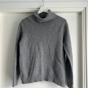 Grå polotröja i ull från Calvin Klein - Mysig grå polotröja från Calvin Klein Collection i barn storlek XXL eller vuxen s. Tröjan är stickad i mjuk ull och har en klassisk polokrage samt ribbade muddar vid ärmslut och nederkant. Perfekt för kyliga dagar och enkel att matcha med jeans eller kostymbyxor.