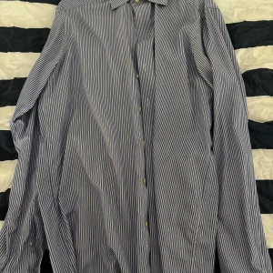 Randig blå skjorta från Eton - Snygg blå- och vitrandig skjorta från Eton i storlek 42. Skjortan har klassisk krage, knäppning framtill och långa ärmar. Tillverkad i bomull och har en modern, stilren look som passar perfekt till jeans eller kostym.