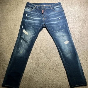 Blå jeans från Dsquared2 - Snygga blå jeans från Dsquared2 med slitna detaljer och en snygg tvätt. De har en klassisk femficksdesign och en röd etikett vid gylfen. Perfekta för en avslappnad stil med en touch av edge. Storlek 48 vilket jag skulle säga passar bra mellan 31-33 i midjestorlek.