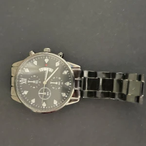 Svart klocka med metallarmband - Stilren svart klocka från Olevs med rund urtavla, datumvisning och flera små urtavlor. Klockan har ett svart metallarmband och silverfärgade detaljer på urtavlan. Perfekt accessoar för dig som gillar en klassisk look.