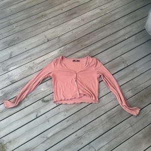 Brun croppad kofta från Bik Bok - Säljer en söt croppad kofta från Bik Bok i en brun nyans. Koftan har långa ärmar, v-ringning och knappar framtill.  Perfekt till lager-på-lager och snygg till både jeans och kjol.