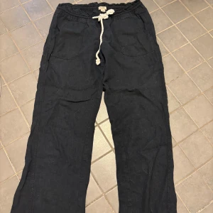 Svarta linnenyxor från Roxy - Svarta linnebyxor från Roxy med avslappnad passform. Byxorna har en vit snörning framtill och stora fickor på sidorna. Perfekta för chill dagar eller strandhäng.