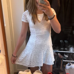 Vit spetsklänning i xxs/xs - Superfin vit kortklänning i spets med rund halsringning och korta ärmar. Klänningen har en figurnära passform upptill och utställd kjol, samt dragkedja i ryggen. Perfekt för sommarens alla tillfällen och ger en romantisk vibe. Jag har vuxit ur klänningen och därför ser den kanske lite liten ut på bilden :)