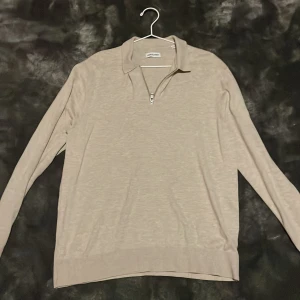 Beige långärmad tröja med half zip - Stilren beige långärmad tröja från J.Lindeberg med krage och half zip-dragkedja. Perfekt för dig som gillar en clean look och vill ha något som funkar till många outfits. Tillverkad i mjukt material som känns skönt mot huden.