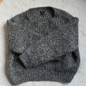 Grå stickad tröja från Lindex - Mysig gråmelerad stickad tröja från Lindex i storlek S. Tröjan har en mysig känsla med grovstickat mönster, rund halsringning och långa ärmar. Perfekt för alla tillfällen,dagar och enkel att styla med jeans eller kjol.