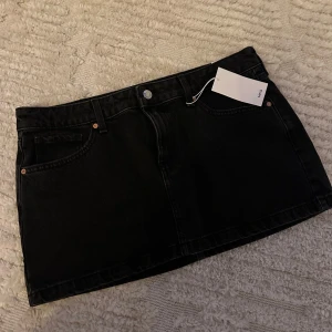 Svart jeanskjol från Mango - Svart kort jeanskjol från Mango med klassisk femficksdesign och bälteshällor. Snygg och enkel modell som är lätt att matcha till olika stilar. Perfekt för dig som gillar en clean och tidlös look. Säljer då den är för stor annars as snygg!