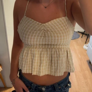 Jättefint beige rutigt linne med volang från Noisy May!💗 - Supersöt beige och vit rutigt linne från Noisy May i storlek S! Tyvärr passar inte den längre så jag måste sälja den. Linnet har volang nedtill och dragkedja på sidan.