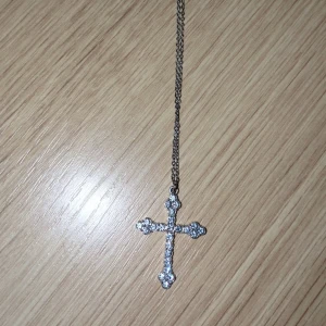 Halsband med glittrigt korshänge - Snyggt halsband med ett korsformat hänge täckt av glittrande stenar. Kedjan är i silver. Perfekt för dig som gillar statement-smycken med lite bling och y2k känsla. 