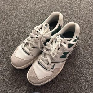 New Balance 550 vita och gröna sneakers - Säljer ett par New Balance 550 sneakers i vitt och grönt. Skorna har klassisk retrodesign med gröna detaljer, snörning och robust sula. Ovandelen är i skinn och mocka med perforerade partier för extra stil. Perfekta för dig som gillar streetwear och sportig vibe.