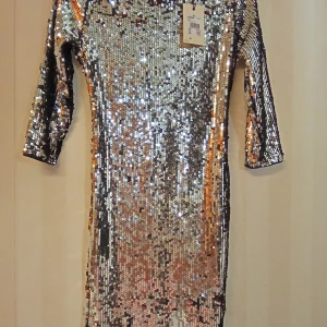 Två super snygga Glittrig silverklänning med Bik Bok märke - Två super snygga glittrig silverfärgad klänningar med Bik Bok märke i storlek M. Klänningar har paljetter över hela, trekvartsärm och en snygg öppen rygg med dragkedja. Tillverkad i 100% polyester och perfekt för er som vill sticka ut. Kan skickas med extra pris via post.