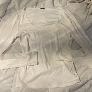 Vit långärmad topp med spetskant - Säljer en vit långärmad topp med rund halsringning och fin spetskant runt urringningen. Tunn och mjuk, perfekt att styla med jeans eller kjol. Enkel men ändå söt detalj med spetsen som ger en romantisk vibe.
