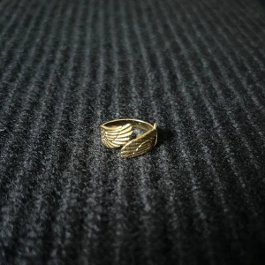 Ailes d’Ange Dorées – Golden Angel Wings Ring - Justerbar ring i rostfritt stål med guldplätering, rost- och nickelfri. Två stiliserade vingar möts i en svepande form – en balanserad kontrast mellan styrka och lätthet