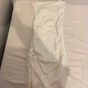 Vit långklänning med slits, pris kan diskuteras  - Snygg vit långklänning i figurnära modell med rynkade sidor och hög slits. Ärmlös design med rund halsringning, perfekt för dig som vill sticka ut. Materialet känns mjukt och stretchigt, vilket ger en smickrande passform. Pris 80kr, ej använd.