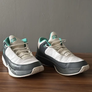 Nike Air Jordan 1 Low vit/turkos - Säljer ett par Nike Air Jordan 1 Low sneakers i vitt och mörkgrått med turkosa detaljer. Skorna har snörning, synlig Air-dämpning i sulan och klassisk Jumpman-logga på sidan. Ovandelen är i skinn och textil, med rund tå och lågt skaft. Perfekt för dig som gillar streetstyle.