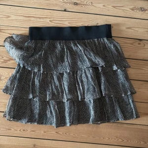 Kort volangkjol med leopardmönster - Supersöt kort kjol med flera volanger och leopardmönster i svart och grått. Kjolen har bred resår i midjan för skön passform och ett flowigt fall. Perfekt för dig som vill sticka ut med en trendig look.