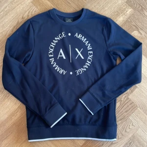 Mörkblå tröja från Armani Exchange - Snygg mörkblå tröja från Armani Exchange med deras ikoniska logga tryckt på framsidan. Tröjan har långa ärmar och en rund halsringning. Perfekt för en stilren och avslappnad look.