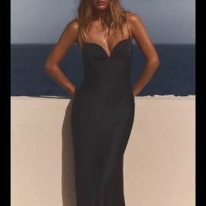 Svart slutsåld långklänning - Elegant svart långklänning med smala axelband och en v-ringad design. Klänningen har en slät och glansig yta som ger en lyxig känsla. Perfekt för en stilren och sofistikerad look. Slutsåld därav priset