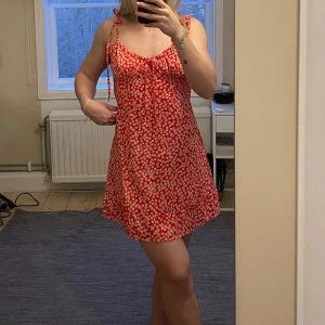 Röd blommig klänning - Säljer en söt röd klänning med vita blommor. Klänningen har smala axelband med knytning😍
