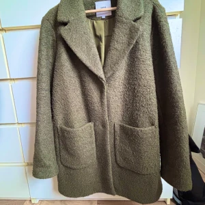 Olivgrön kappa från ICHI - Snygg olivgrön kappa från ICHI med en klassisk design. Den har långa ärmar och två stora fickor framtill. Perfekt för höst och vår med sin stilrena look.