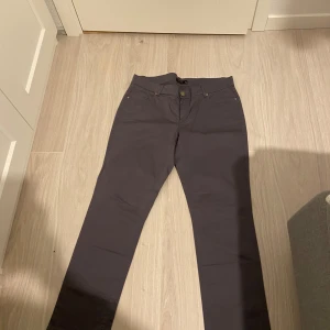 Grå byxor från Lindex - Snygga grå byxor från Linx med normal passform. Byxorna har en klassisk design med knappar och dragkedja framtill. Perfekta för en stilren look.