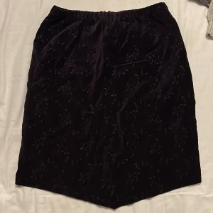 Lila blommig kjol - Söt lila kjol i sammetstyg med blommönster. Smickrande passform och gott skick