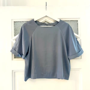 Blå topp i glansigt material  - Blå oversized T-shirt i silke/sidenmodell. Glansigt fint tyg som faller snyggt på kroppen. 
