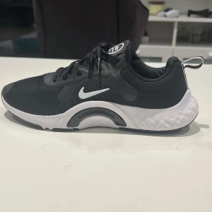Svarta Nike skor - Snygga svarta Nike sneakers med vit sula och klassisk snörning. Skorna har en sportig design med en liten Nike-logga på sidan och texten 'Just Do It' på plösen. Perfekta för en aktiv livsstil.