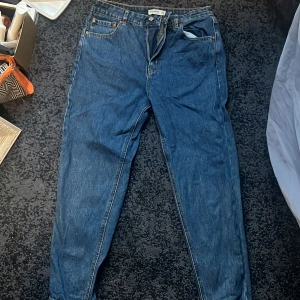 Blå jeansbyxor - Säljer ett par klassiska blå jeansbyxor med låg midja och en straight passform. Byxorna har fem fickor och stängs med dragkedja och knapp. Perfekta för en avslappnad stil. STORLEK 38