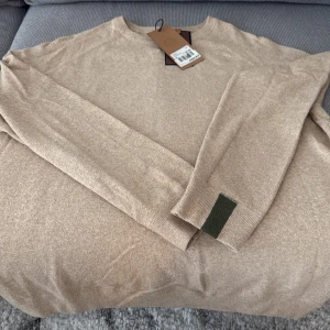 ”Kyle soft knit” från Mos Mosh - Säljer en stilren beige tröja med en grön detalj vid ärmslutet. Tröjan har långa ärmar och är perfekt för en avslappnad look. Passar bra till både jeans och chinos. Köpt för ett tag sedan men har bara hängt kvar i garderoben således oanvänd och med lappar kvar. Strl XL men skulle snarare säga M/L. Nypris 1399kr.