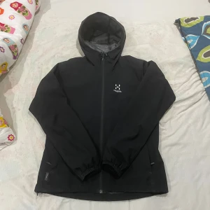Haglöfs jacka - Säljer en svart vindjacka från Haglöfs i storlek S för dam. Jackan har en praktisk huva och dragkedja framtill. Perfekt för blåsiga dagar och har fint utseende med Haglöfs logga på bröstet.