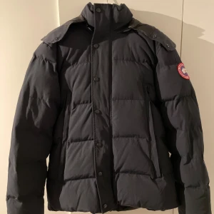 Navy vinterjacka från Canada Goose - Säljer en mörkblå vinterjacka från Canada Goose med avtagbar huva och pälsdetalj. Jackan har långa ärmar och stängs med dragkedja och knappar. Perfekt för kalla vinterdagar. Säljer pga varmare årstider! OBS!!! PRIS KAN DISKUTERAS!!!
