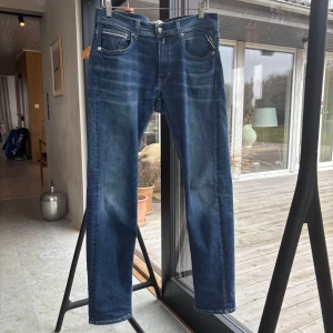 Blå jeans från Replay - Snygga blå jeans från Replay med klassisk femficksdesign och knappgylf. Jeansen har en modern passform och är perfekta för en avslappnad stil. Märkesdetaljer på baksidan och knappen ger en extra touch.