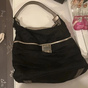Svart axelväska från Calvin Klein - Snygg svart axelväska från Calvin Klein med silverfärgade detaljer och dragkedja. Väskan har en stilren design med praktiska fack och en bekväm axelrem. Perfekt för att bära med sig det nödvändigaste med stil. Vintage❤️