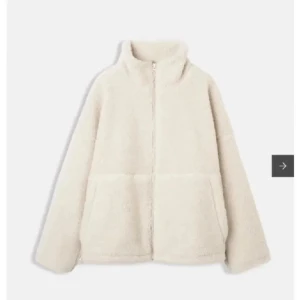 Beige teddyjacka med dragkedja - Mysig beige teddyjacka med dragkedja och hög krage. Perfekt för kyliga dagar med sin fluffiga och varma design. Jackan har långa ärmar och två praktiska fickor framtill.