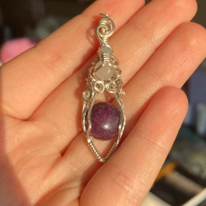 Halsband med lila och rosa stenar - Unikt halsband med en lila sten och en mindre rosa sten, inramade i en detaljerad silverfärgad metallinfattning. Perfekt för att ge en elegant touch till din outfit.