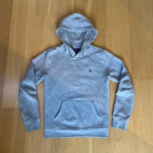 Grå hoodie från Ralph Lauren - Säljer en grå hoodie från Ralph Lauren med det ikoniska broderade logotypen på bröstet. Tröjan är super bekväm! Och har en fantastisk passform med långa ärmar och en praktisk magficka. Perfekt för en avslappnad stil. Storlek S-M