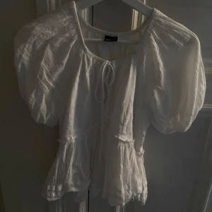 Vit blus från Gina Tricot - Säljer en söt vit blus från Gina Tricot i storlek XS. Blusen har korta puffärmar och en knytning framtill.  Lite trådar nere på blusen men den ska vara så❣️