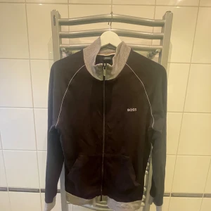 Svart och grå jacka från Boss - Säljer en stilren svart och grå jacka från Boss. Jackan har en dragkedja framtill och långa ärmar. Perfekt för en casual look.