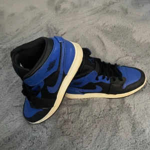 Svart och blå Nike Air Jordans - Snygga Nike Air Jordans i svart och blått med klassisk snörning. Skorna har en hög design och är perfekta för dig som vill ha en stilren look med en sportig touch. Ny pris 3000
