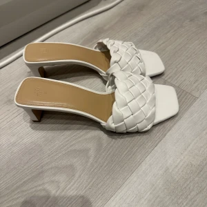 Vita flätade klackskor - Snygga vita klackskor med flätad ovandel och fyrkantig tå. Perfekta för en stilren look. Klacken är medelhög och ger en elegant touch.