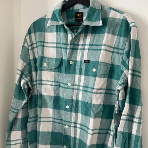 Grön/vit rutig overshirt från Lee - Säljer en grön och vit rutig skjorta från Lee i storlek M. Skjortan har en avslappnad passform med långa ärmar och knappar framtill. Två bröstfickor med knappstängning ger en klassisk look. Perfekt för en avslappnad stil eller för att elevate som overshirt framåt vår/sommar. Nypris: 899kr.