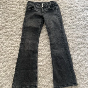 Svarta jeansbyxor från Gina Tricot - Snygga svarta jeansbyxor från Gina Tricot med bootcut-stil. Byxorna har två knappar fram och klassiska bakfickor med knappdetaljer. Perfekta för en trendig look.