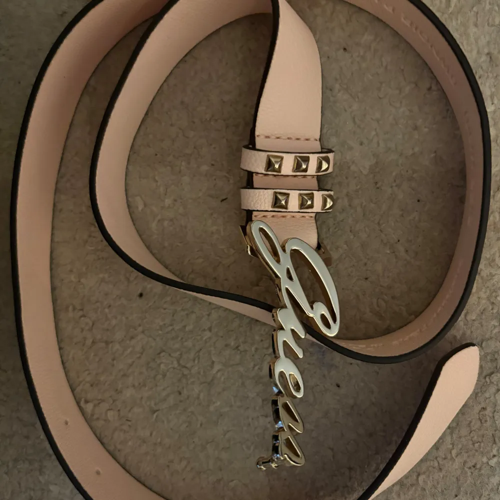 Snyggt rosa bälte från Guess med guldfärgad logotyp och nitar. Perfekt för att ge din outfit en extra touch. Tillverkad i skinn med stilrena detaljer.. Muu.