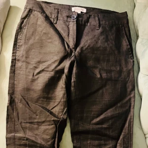 MNG Basics lågmidjade, svarta linnebyxor  - Snygga svarta byxor från MNG Basics med knapp och dragkedja framtill. Byxorna har en klassisk design med fickor både fram och bak, vilket ger en stilren look. Perfekta för en elegant och tidlös stil.