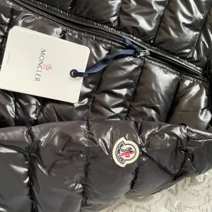 Moncler vårjacka - Snygg svart pufferjacka från Moncler med quiltad design och dragkedja framtill. Jackan har en hög krage och två praktiska fickor med dragkedja. Perfekt för kyligare dagar.