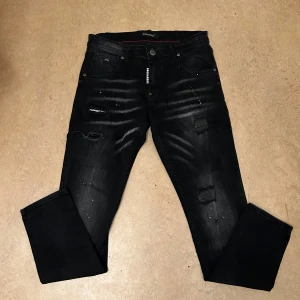 Svarta Dsquared2 Jeans - Snygga svarta jeans från Dsquared2 med coola slitningar och detaljer. Jeansen har en normal passform och är perfekta för en trendig look. De har en klassisk femficksdesign och en unik etikett på baksidan.